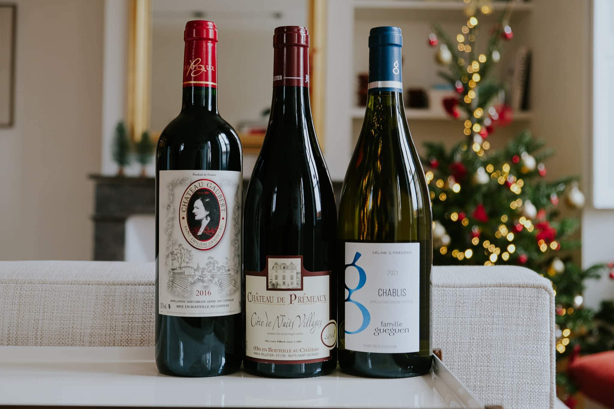 Sélection de trois vins français : Bordeaux Saint-Émilion 2016, Côte de Nuits Villages 2018 et Chablis 2021. Décor de Noël.